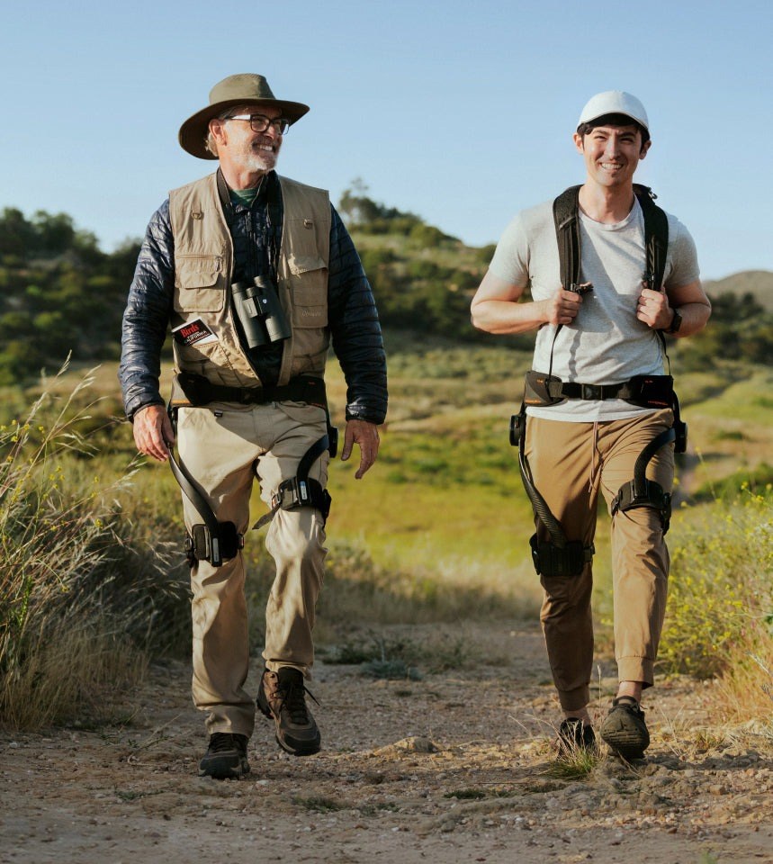 Two hikers wearing the Hypershell hiking exoskeleton on a sunny trail