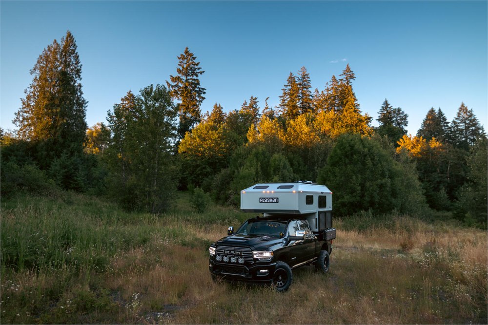 Alaskan HS 640 camper parked in a field with forest around it