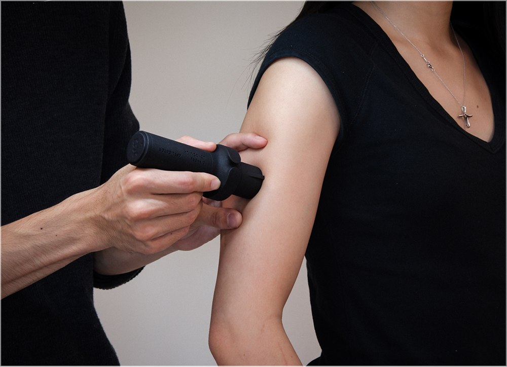 A black applicator pressing a tiny Microdot Tattoo patch onto an upper arm