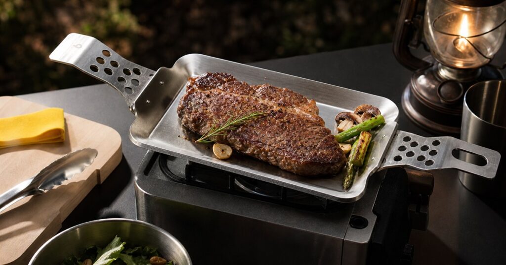 Compact modular grill plate cooking steak on a portable burner