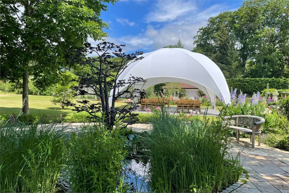 DreamDomes Crossover L dome set up in a landscaped garden with dining tables