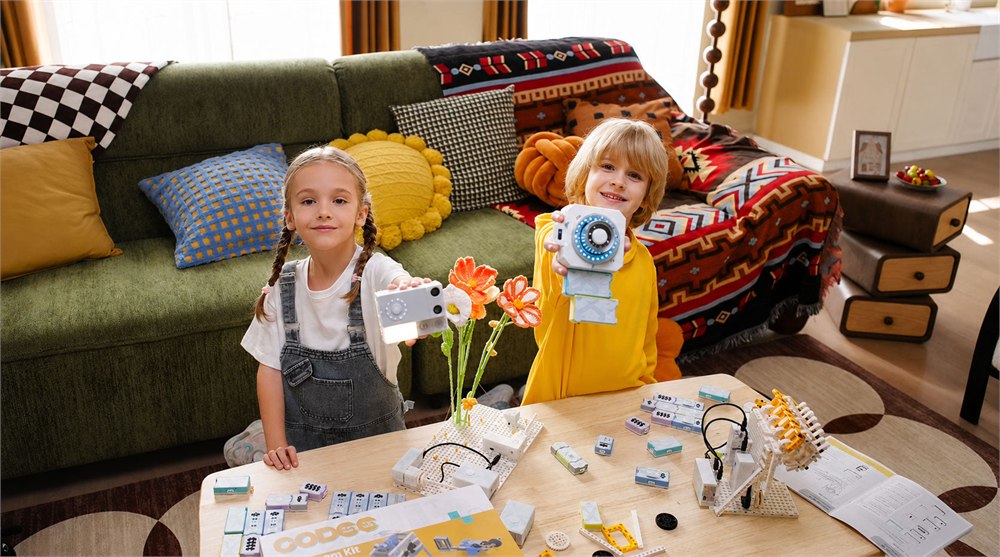 Kids holding CODEE controller pieces at a table full of robot parts