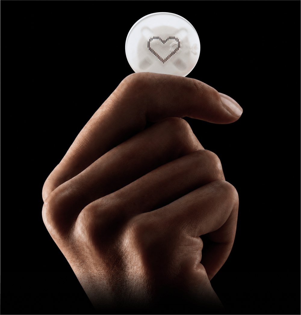 A fingertip holding a circular Microdot Tattoo patch with a dotted heart design