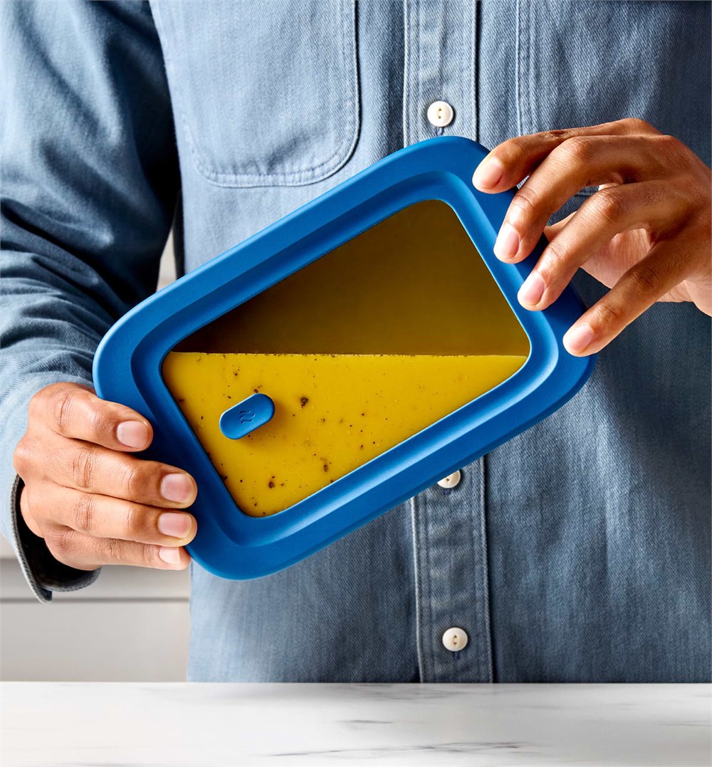 Blue silicone and glass Misenware universal lid being held over food