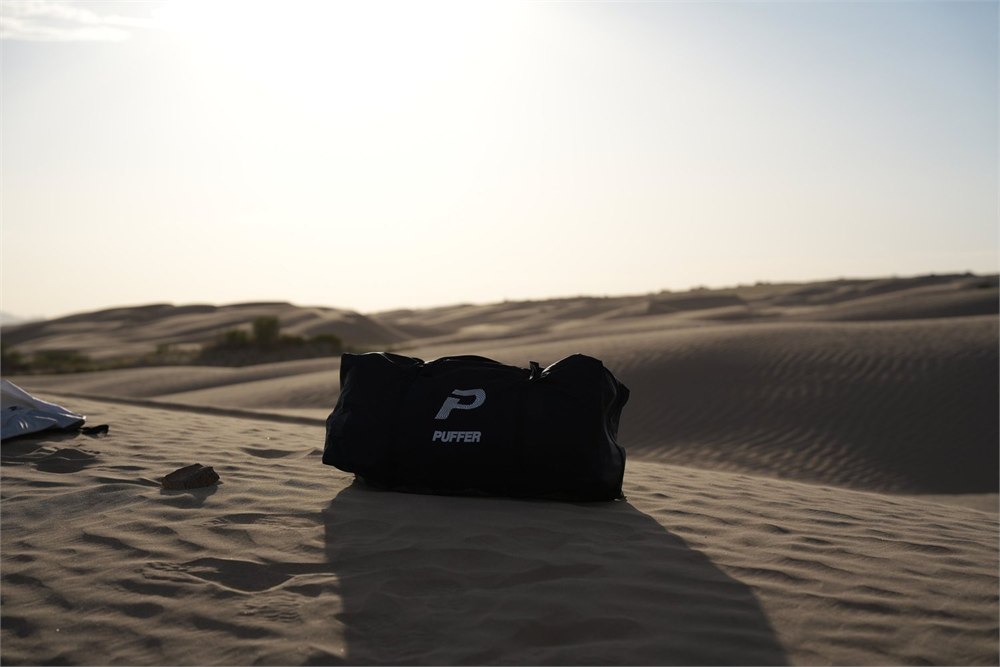 Puffer duffel bag sitting on desert sand before setup