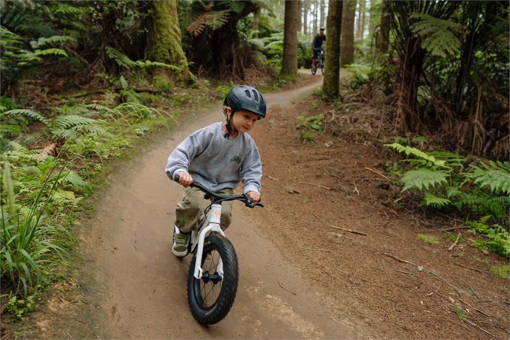 Child riding a white balance bike on a forest trail before it can be carried in the Uplift backpack