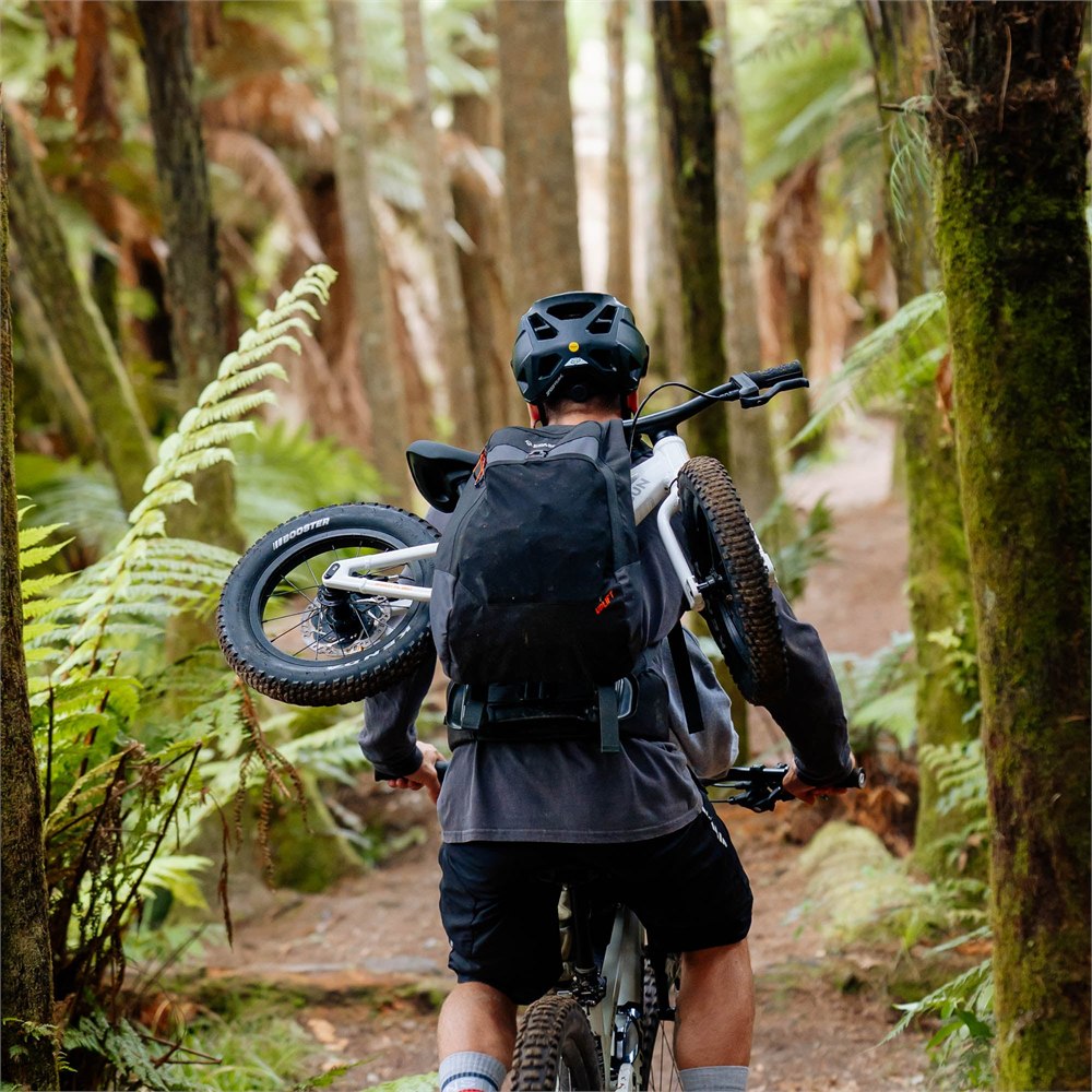 Adult carrying a child balance bike on the Uplift backpack while walking a forest trail
