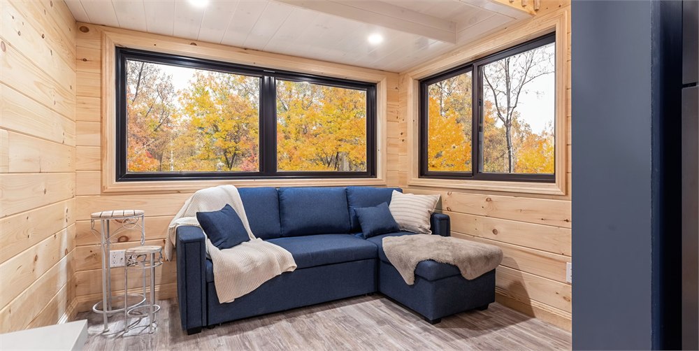 White Pine tiny house living area with sofa bed, windows, and wood interior