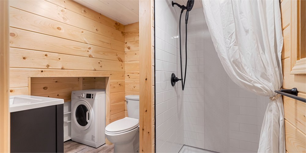 White Pine tiny house bathroom with shower, toilet, vanity, and compact laundry area