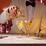 A bartender pouring from the double pour mixing glass into two martini glasses
