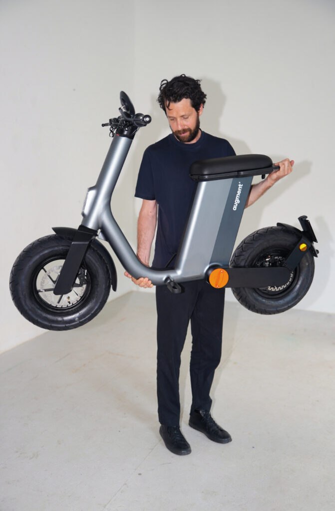 Person carrying the Augment 360 folding electric moped to show its scale