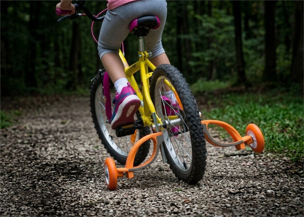 Child leaning a bicycle with Baswil flexible training wheels installed