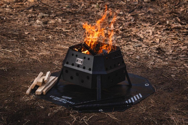 FIRE PIT MAX burning on a protective fire shield mat with firewood nearby