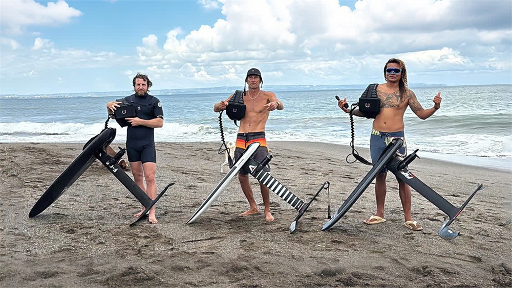 Foildash riders holding hydrofoil boards and battery harnesses on the beach
