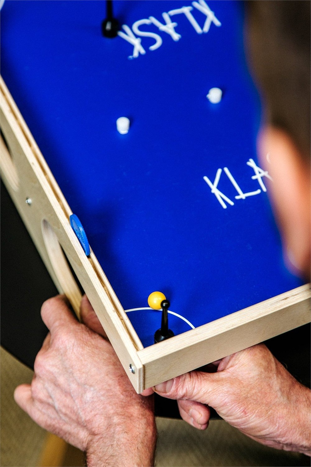 Close-up of the blue KLASK playfield with magnetic strikers, ball, and white obstacles