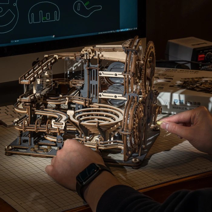 Hands adjusting a ROKR wooden marble run module beside instructions and packaging