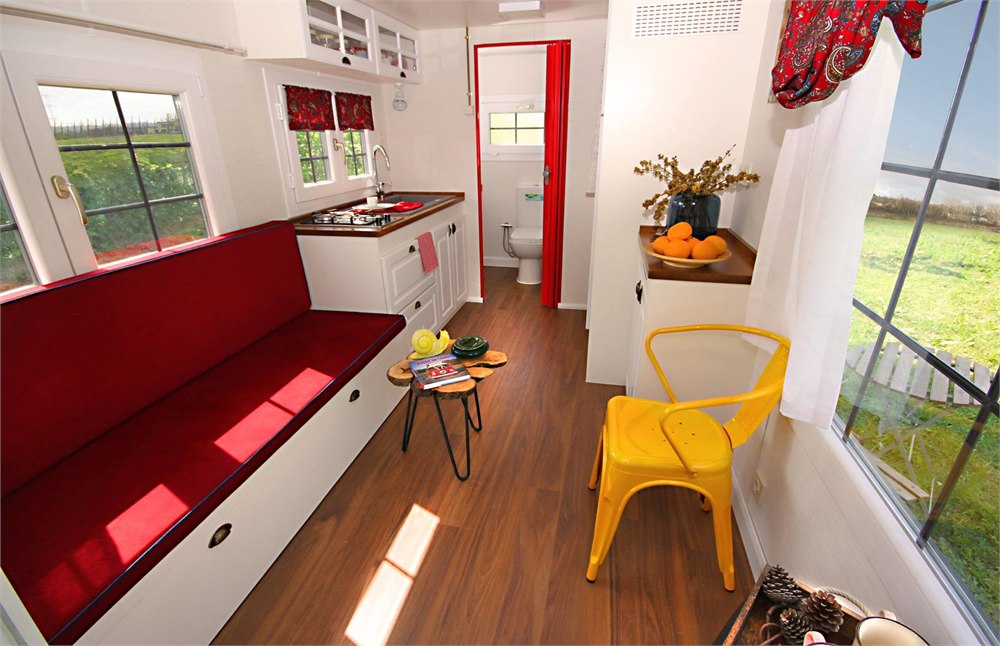 Interior living area of the Saly Sunrise tiny house with red sofa bed and kitchen