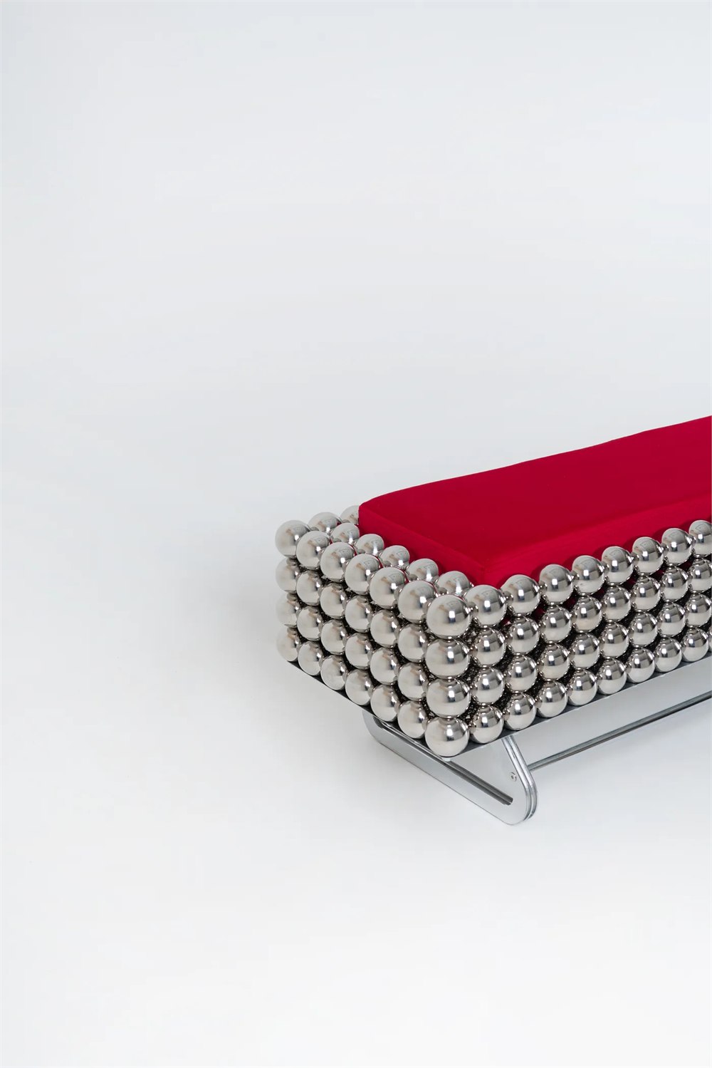 Close view of the Wishes Collection reflective steel sphere furniture with a red cushion