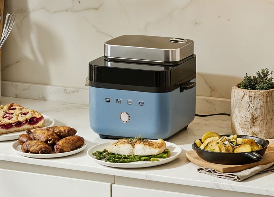 Storm Blue SMEG air fryer on a kitchen counter with prepared dishes