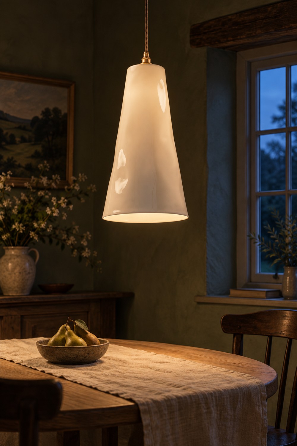 Glowing tapered bone china pendant with a brass fitting above an oak dining table in an olive-green room at dusk.