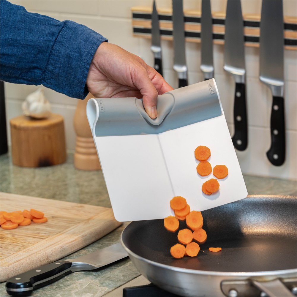 Folding food scooper tipping carrot slices into a pan