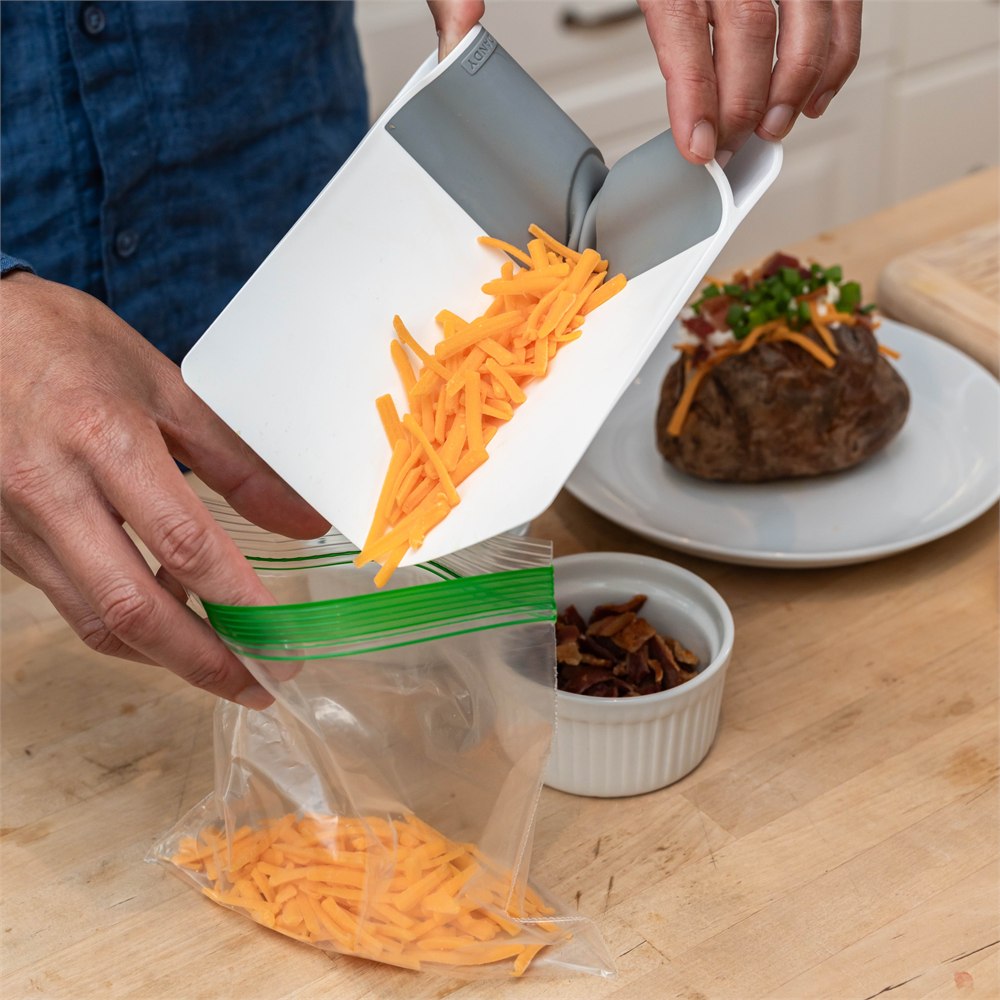 Food scoop funneling grated cheese into a storage bag