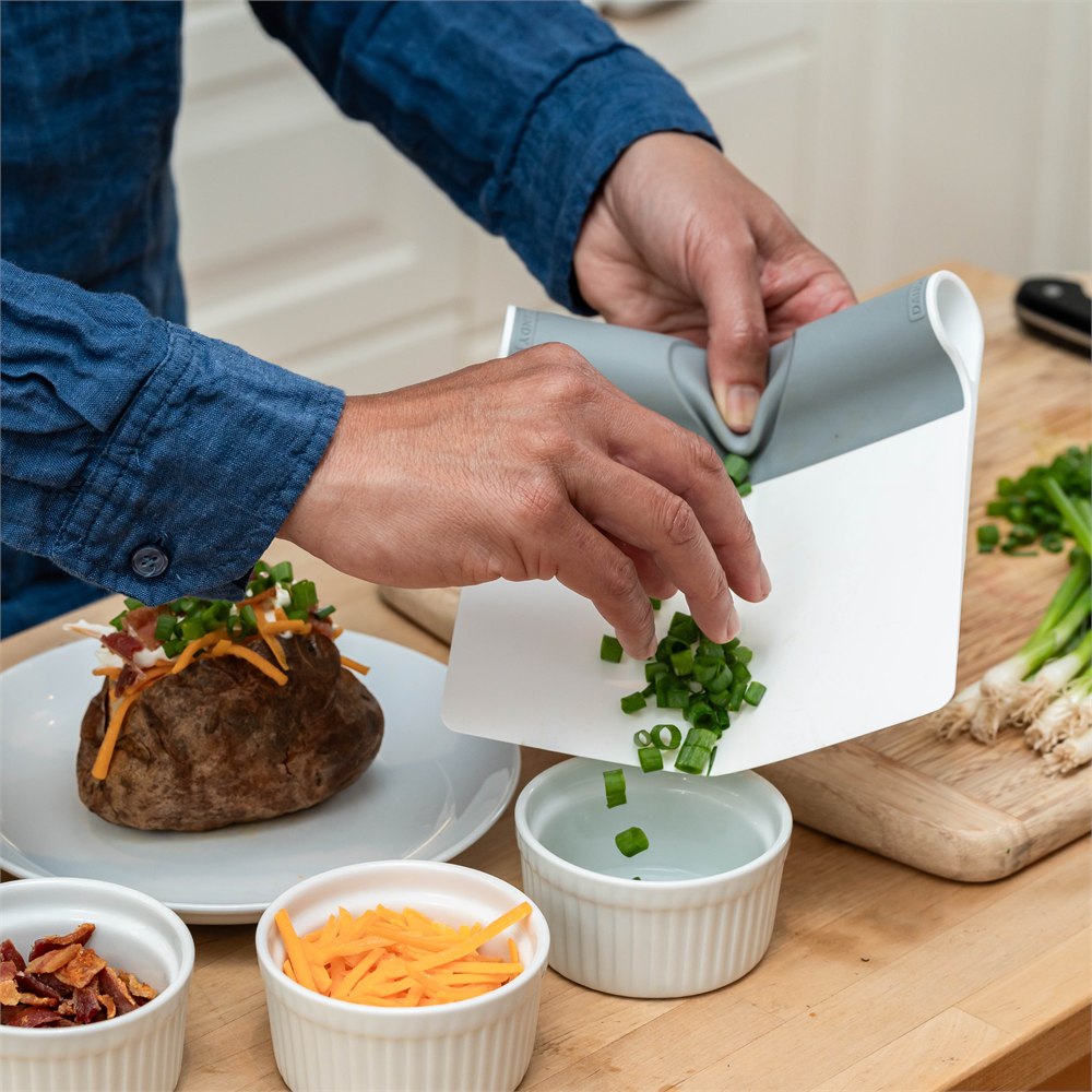 Flexible food scoop directing chopped chives into a ramekin