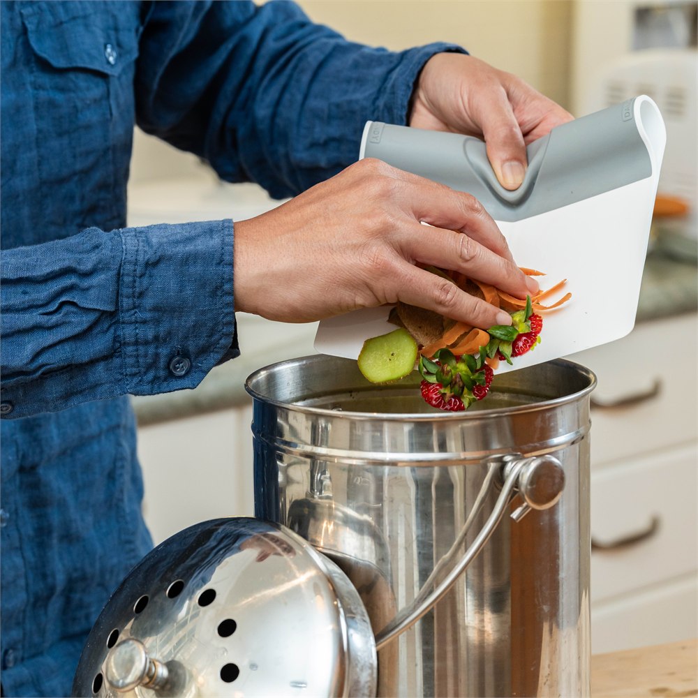 Folding scooper carrying vegetable scraps to a compost bin