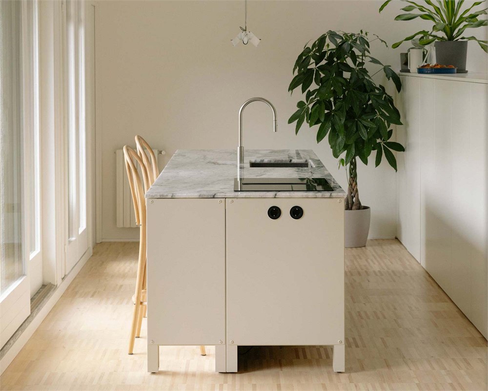 Pale kitchen island with sink and cooking surface beside a dining area