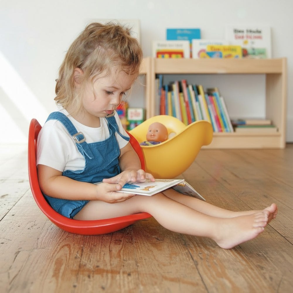 Red MOLUK Bilibo being used as a reading seat and pretend cradle.