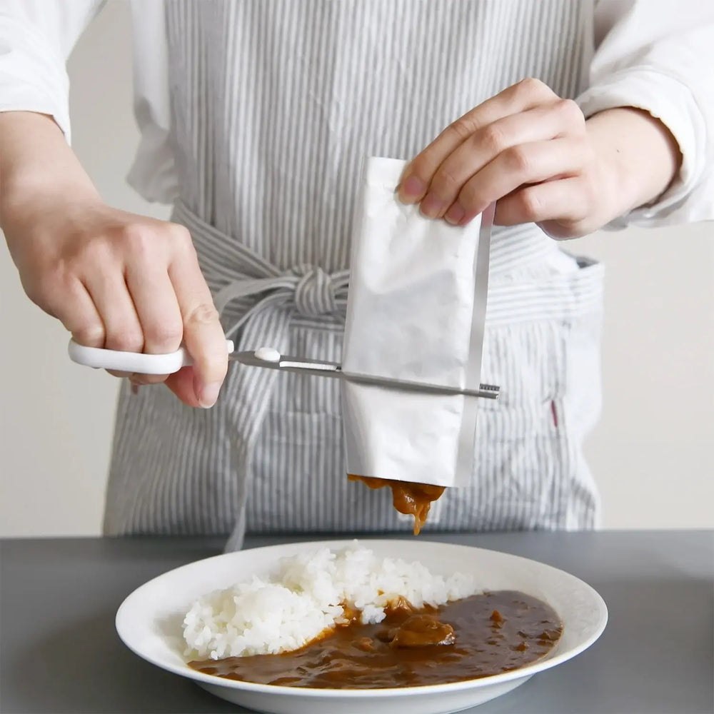 Food pouch scissors pressing curry from a silver packet onto rice
