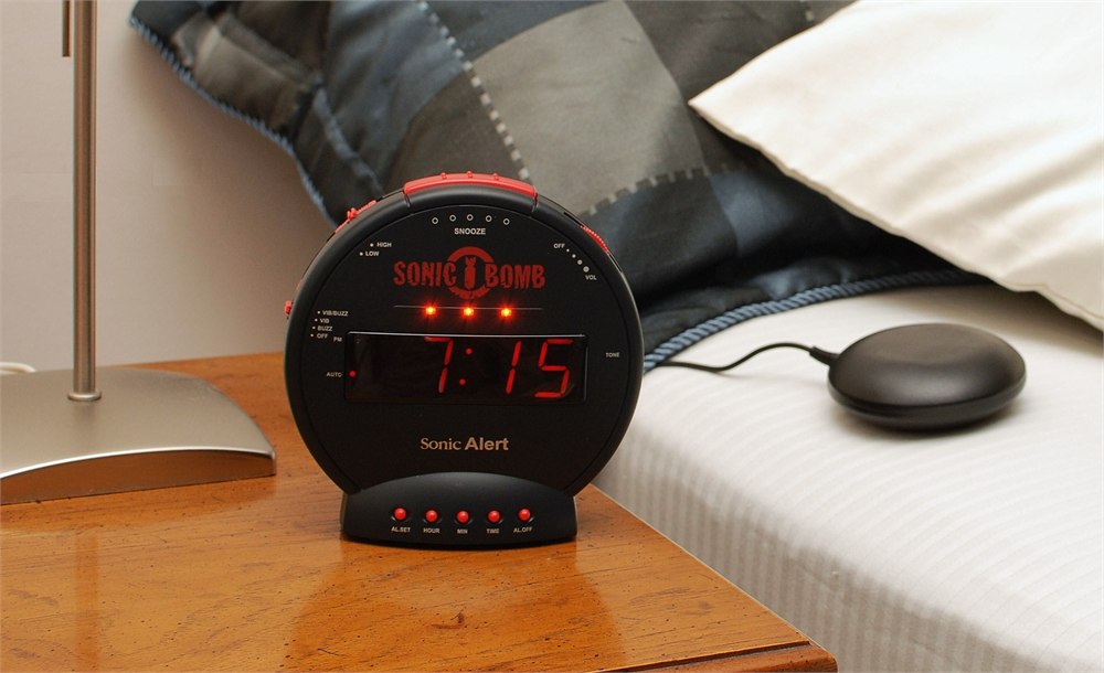 Sonic Bomb alarm clock with bed shaker puck beside bedding