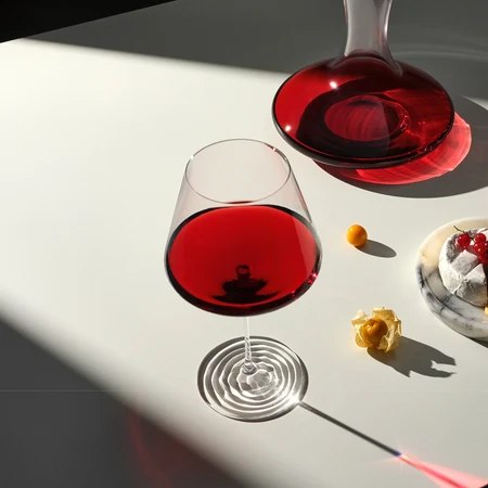 Splash red wine glass beside a carafe in sunlight