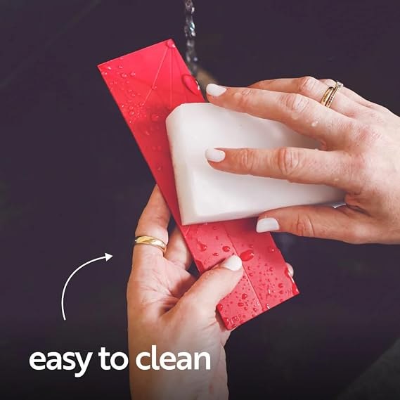 An unfolded red measuring spoon being washed with a sponge