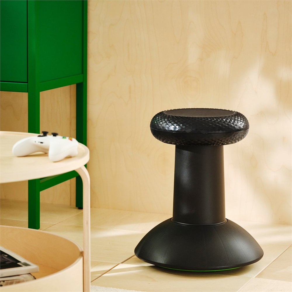 Black YXSTABY thumbstick-inspired stool placed beside a gaming setup with controller and side table