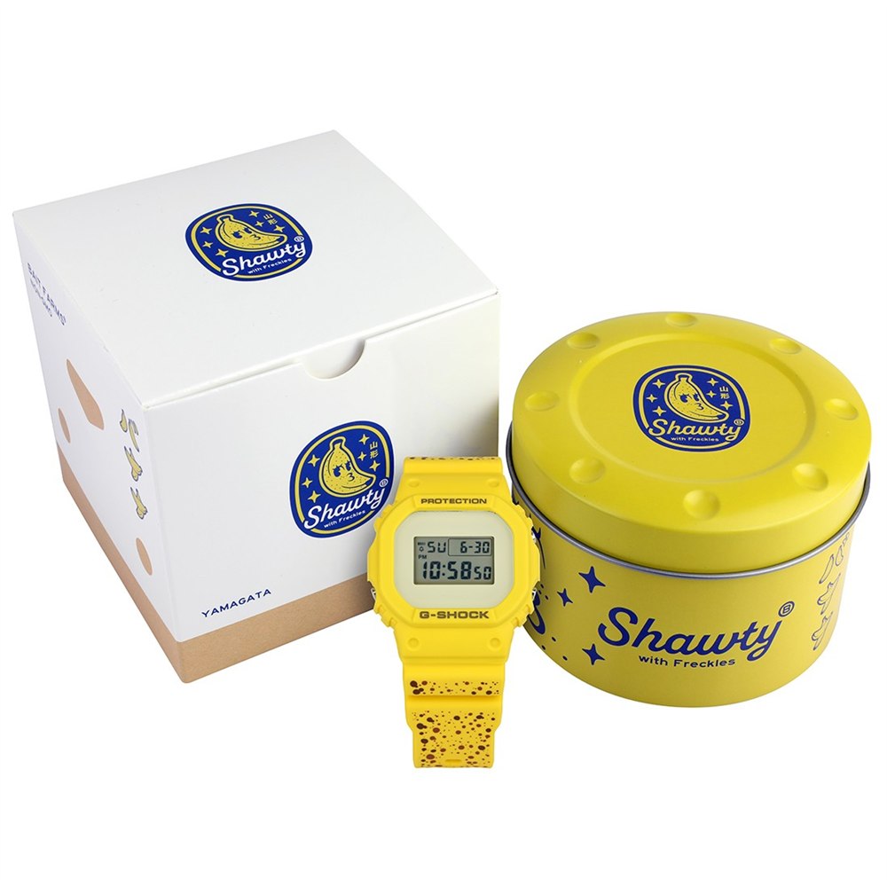 Banana watch beside its yellow tin and illustrated box