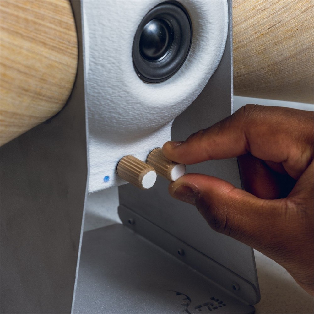 Hand adjusting a wooden control knob below the central speaker driver
