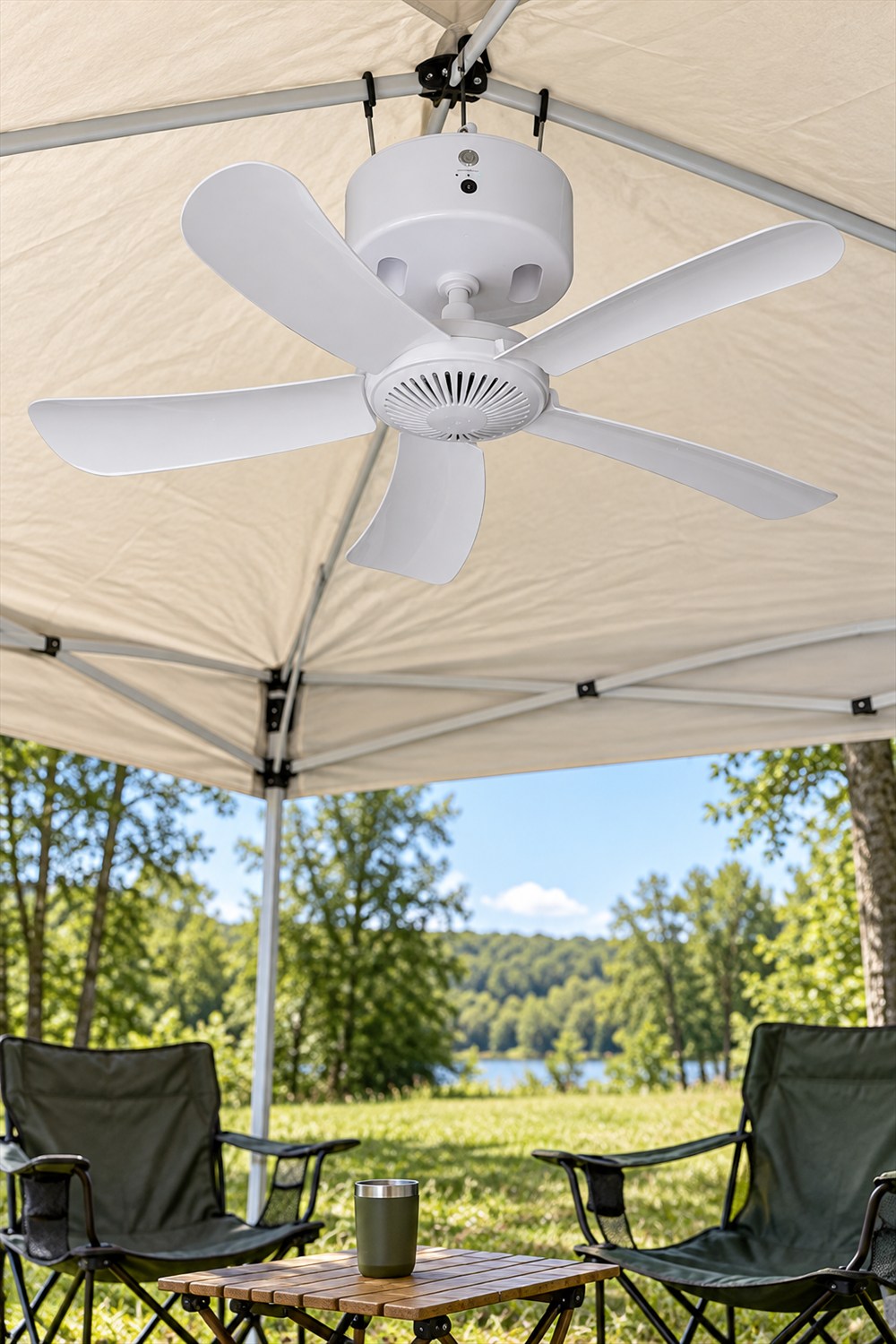 White five-blade Canopy Breeze fan hooked beneath a pop-up canopy above two folding chairs and a camping table.