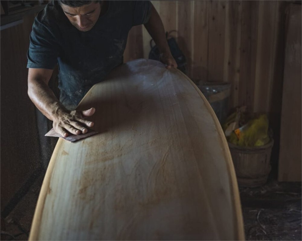 Craftsperson hand-sanding a wooden surfboard
