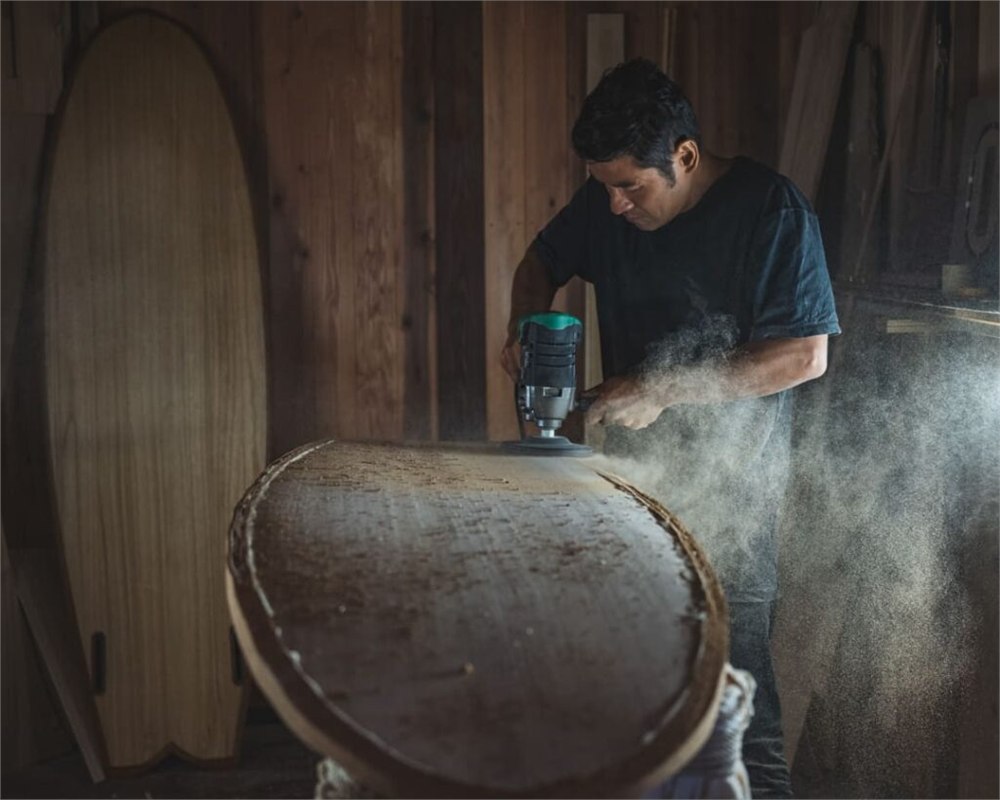 Craftsperson shaping a wooden surfboard with a power tool