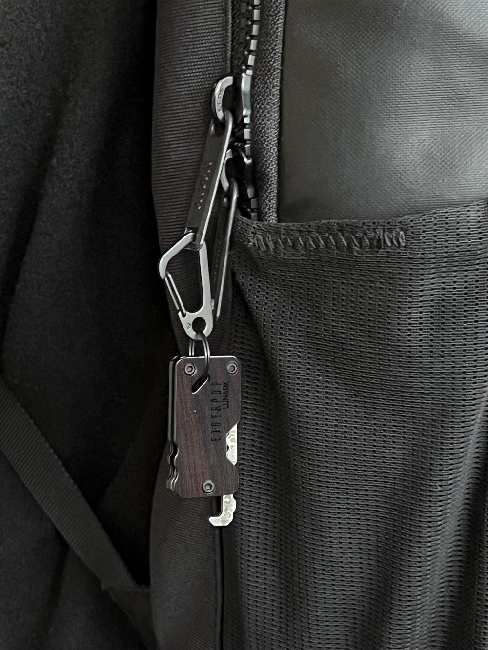Edge & Pop knife attached to a black backpack with a mini carabiner clip.