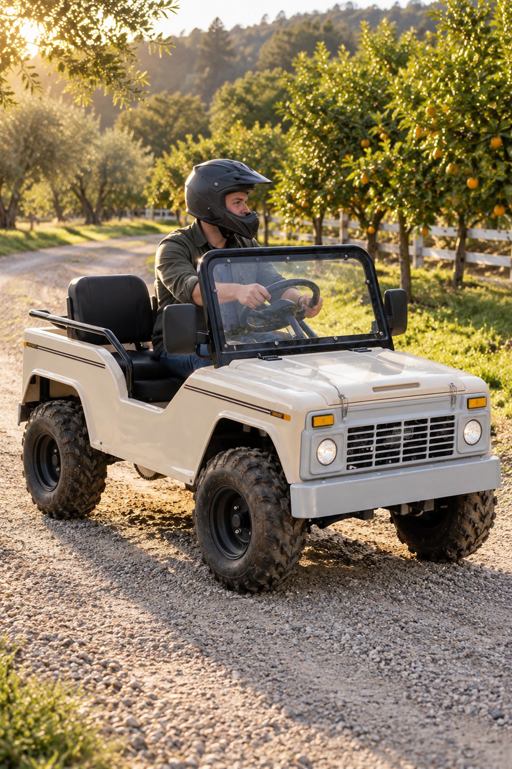 Cream Massimo Mini Truck go-kart with a helmeted adult driver and empty passenger seat on a gravel lane beside a sunlit orchard.