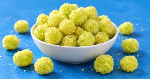 Yellow-green dill pickle corn puffs in a white bowl on a blue tabletop