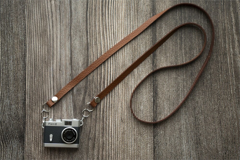 Black Pieni III camera with its neck strap on a wooden surface