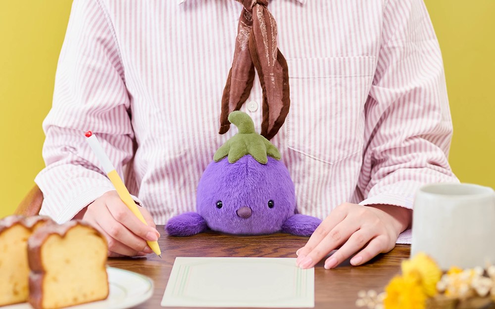 Purple eggplant posture plush at a writing desk