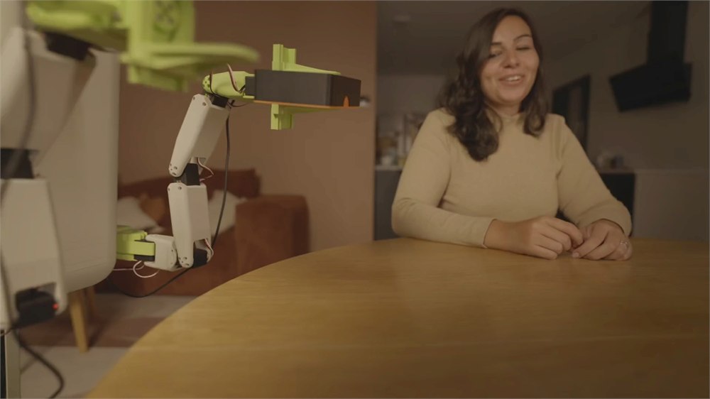 Flourish robot reaching toward a table beside a seated woman