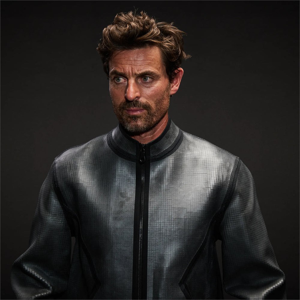 Model wearing the charcoal Vollebak Rock Jacket with a slate tile surface