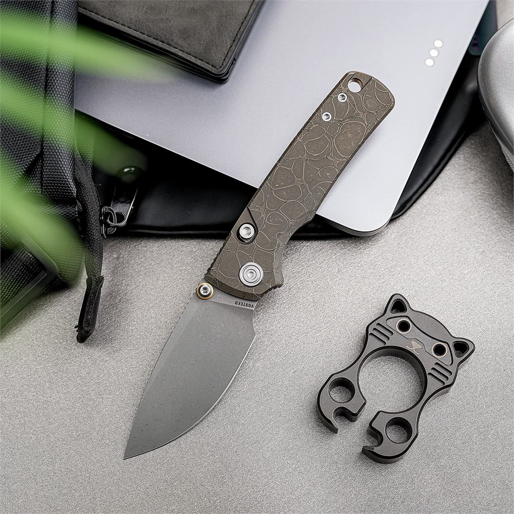 Patterned titanium folding knife on a desk beside everyday accessories